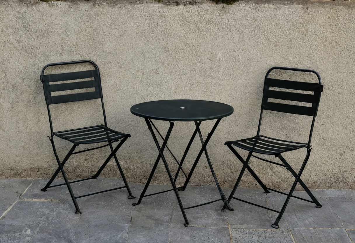 Two open black metal chairs face a small round black table on gray stone paving beside a plain wall.